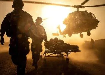 Soldaten transportieren einen Verletzten auf einer Trage zu einem landenden Rettungshubschrauber im Sonnenuntergang. Das Bild symbolisiert extreme Stresssituationen und zeigt, wie ruhiges Handeln unter Druck Leben retten kann – eine Fähigkeit, die auch Operationstechnische Assistenten (OTAs) im OP beherrschen müssen.