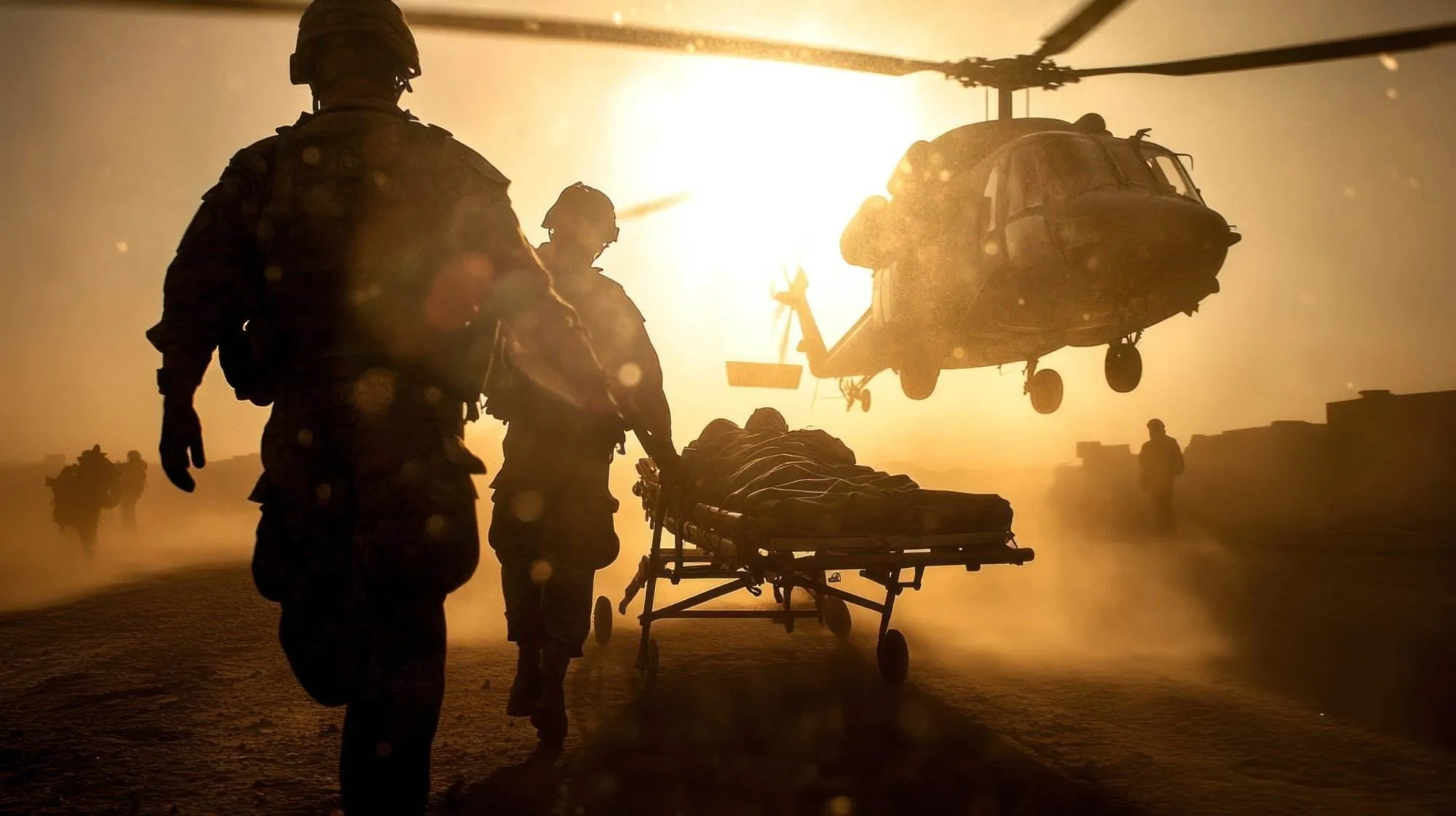 Soldaten transportieren einen Verletzten auf einer Trage zu einem landenden Rettungshubschrauber im Sonnenuntergang. Das Bild symbolisiert extreme Stresssituationen und zeigt, wie ruhiges Handeln unter Druck Leben retten kann – eine Fähigkeit, die auch Operationstechnische Assistenten (OTAs) im OP beherrschen müssen.