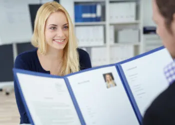Eine junge Bewerberin im erfolgreichen Bewerbungsgespräch für die OTA Ausbildung, während der Personaler ihre Bewerbungsunterlagen prüft.