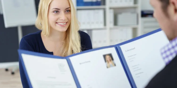 Eine junge Bewerberin im erfolgreichen Bewerbungsgespräch für die OTA Ausbildung, während der Personaler ihre Bewerbungsunterlagen prüft.