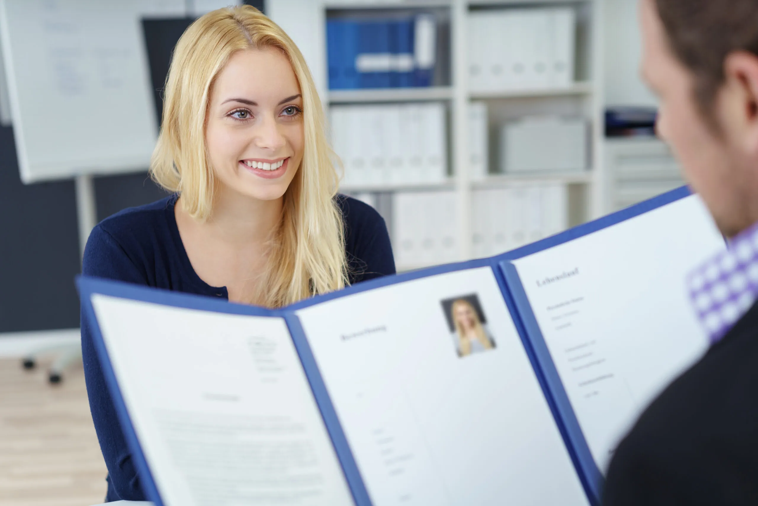 Eine junge Bewerberin im erfolgreichen Bewerbungsgespräch für die OTA Ausbildung, während der Personaler ihre Bewerbungsunterlagen prüft.